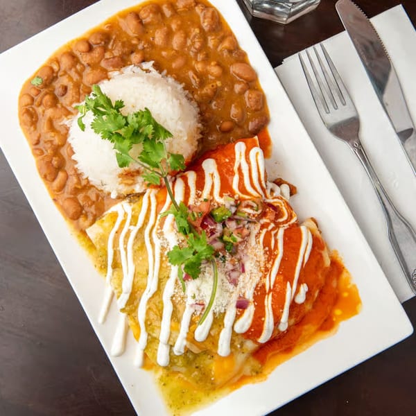 A plate of enchiladas with red and green sauce, rice, and beans, garnished with cilantro.