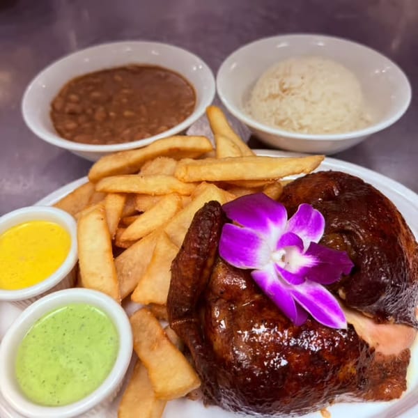Roasted chicken with fries, two dipping sauces, rice, and beans, garnished with a purple orchid.