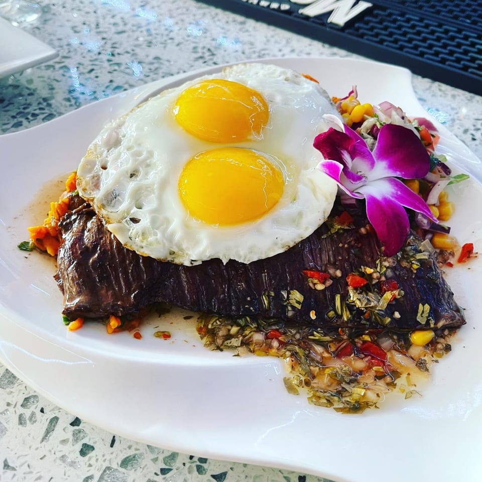 Peruvian/Mexican bar-&-grill dish with steak, two fried eggs, salsa, and an orchid garnish.
