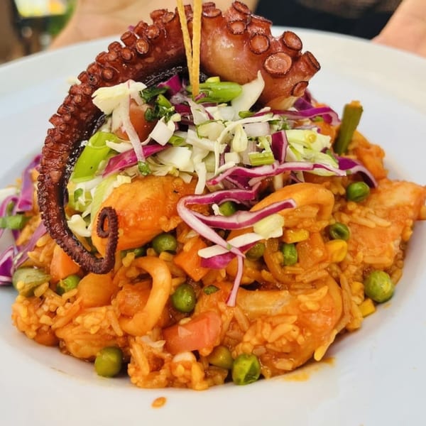 Peruvian-Mexican seafood rice dish with octopus, calamari, shrimp, and vegetables, topped with fresh slaw.