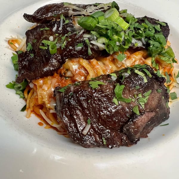 Peruvian-Mexican Fusion Bar and Grill's dish with dark meat, noodles, red sauce, and green onions.