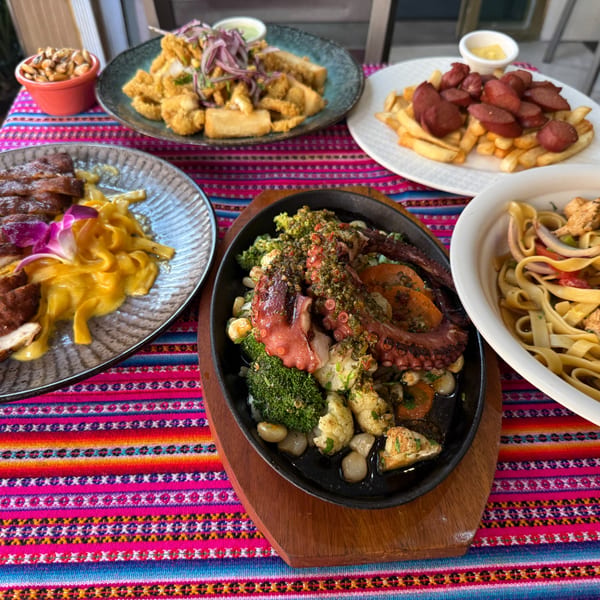 A vibrant table spread with various Peruvian dishes, including octopus, fried calamari, and pasta.