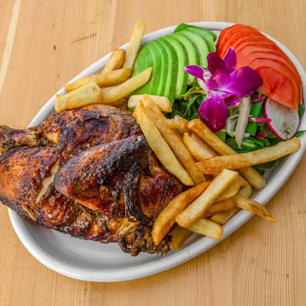 Grilled chicken with french fries, sliced avocado, tomato, and a purple orchid garnish on a white plate.