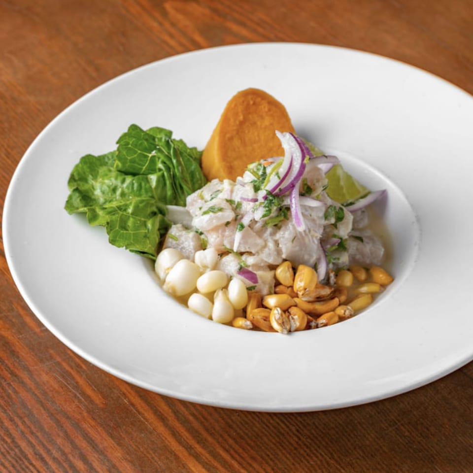 Peruvian ceviche with fish, red onion, corn, sweet potato, and lettuce on a white plate.