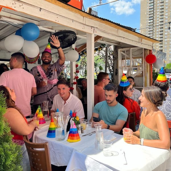 Friends celebrating a birthday with colorful party hats and balloons at an outdoor restaurant.